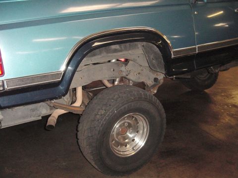 1984 Ford Bronco - The rear suspension and wheel well of a vehicle are visible, with a portion of the exhaust pipe also in view.