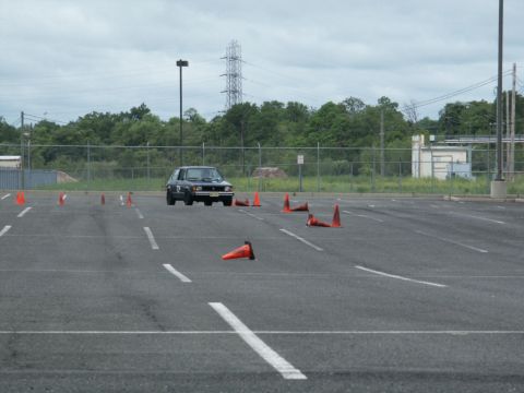 2001 Mercury Grand Marquis - A dark hatchback navigates a cone course in an empty parking lot under an overcast sky.