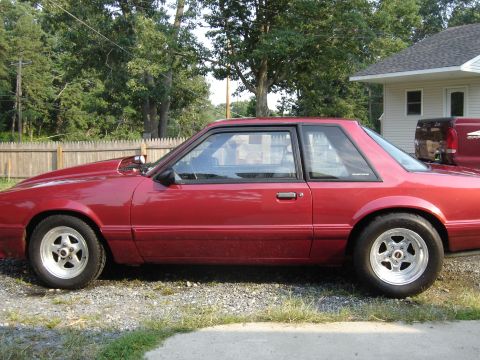 1988 Ford Bronco - A red coupe with a prominent hood scoop and drag racing tires is seen from the side.