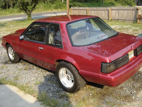 1988 Ford Bronco - A red coupe, likely a Ford Mustang from the late 1980s, is parked outdoors with prominent drag racing tires.