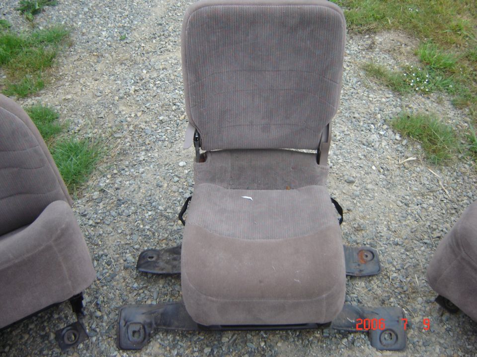 Brown cloth vehicle seat with mounting rails sitting on gravel outdoors