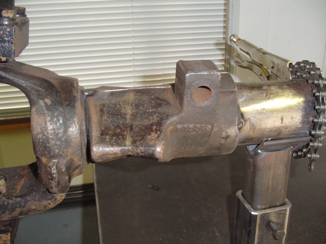 Cast steel joint welded to a shaft, held in a repair stand with vise grips and chain in background