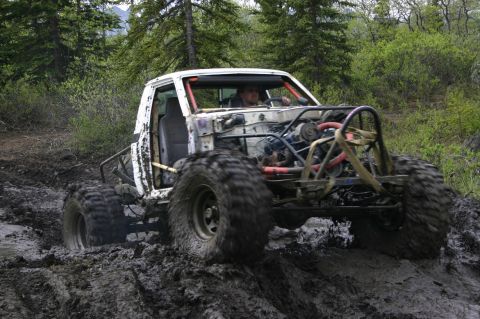 2003 Jeep TJ - A modified off-road vehicle navigates a muddy trail in a wooded area.