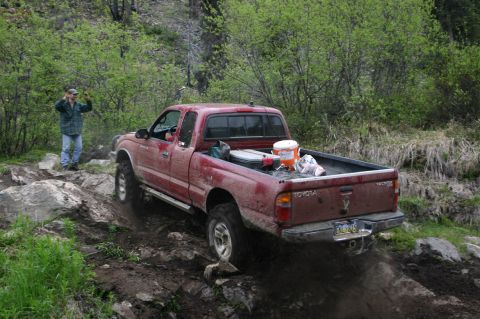 2003 Jeep TJ - A red 2003 Toyota Tacoma navigates a challenging off-road course with a person watching.