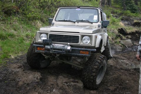 2003 Jeep TJ - Suzuki Samurai navigates a challenging off-road course with steep inclines and mud.