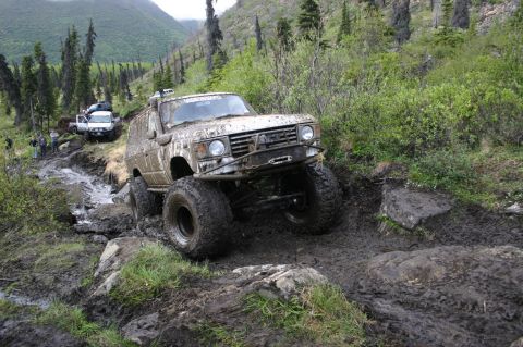 2003 Jeep TJ - This heavily modified SUV is tackling a challenging off-road course, covered in mud from the difficult terrain.