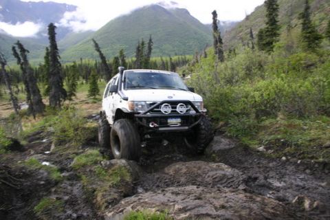 2000 Ford E350 - Modified SUV tackling a challenging off-road course in a mountainous, wooded area.