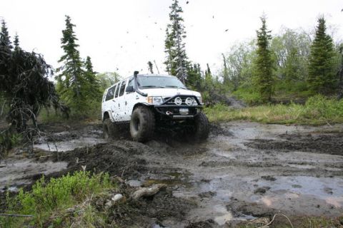 2000 Ford E350 - A white SUV navigates a challenging muddy terrain with trees in the background.
