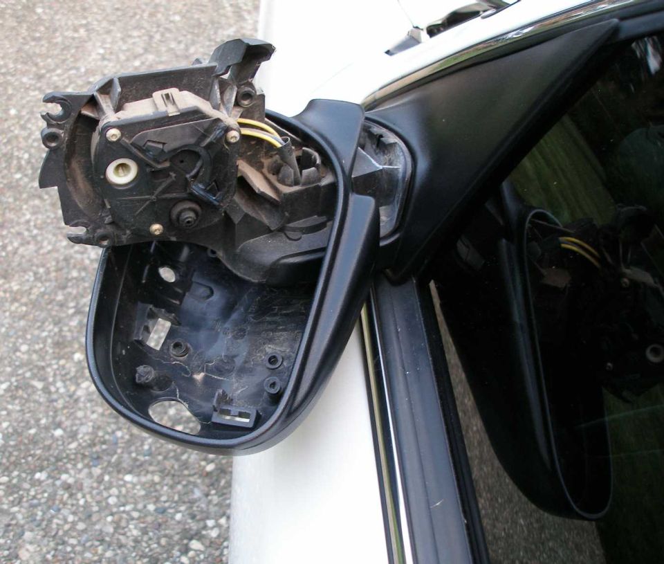 Disassembled black side mirror with exposed motor on white sedan