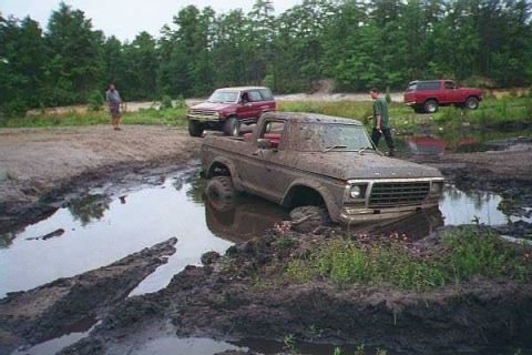 1990 Ford Bronco - A muddy 1979 Ford F-Series pickup truck is stuck in a mud pit, with a red SUV visible in the background.
