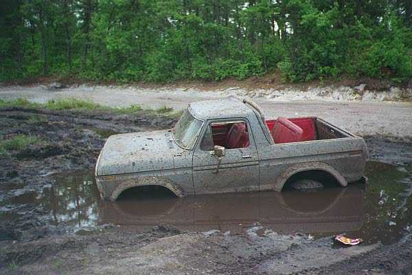 Old pickup truck stuck in a mud pit with trees in the background