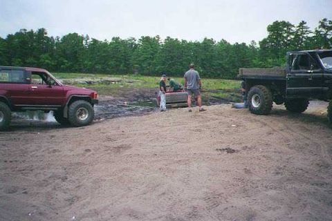 1990 Ford Bronco - Two off-road vehicles are parked on a dirt lot with several people nearby.
