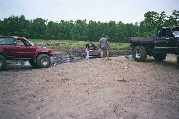 Red SUV and black pickup truck on dirt with people standing around