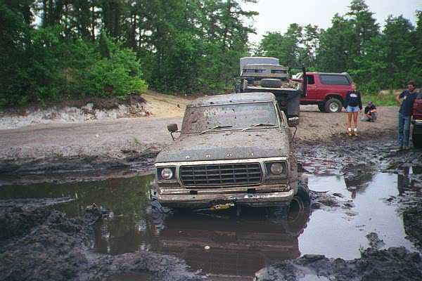 Ford F-Series truck stuck in mud, other vehicles and people in background