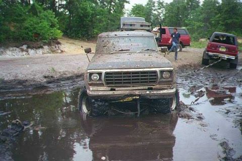 1990 Ford Bronco - This heavily mud-caked 1979 Ford F-Series truck is stuck in a muddy pit with another vehicle visible in the background.