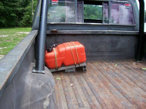 1990 Ford Bronco - The interior of a truck bed shows an orange auxiliary fuel tank secured with ropes, with Holley stickers on the rear window.