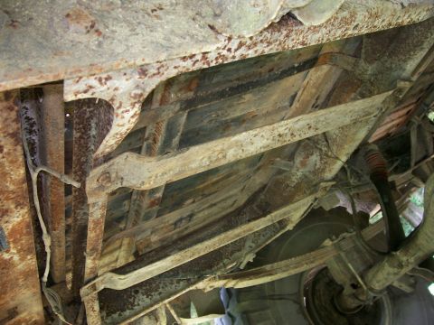 1990 Ford Bronco - The heavily rusted undercarriage of a vehicle, revealing its frame and suspension parts.