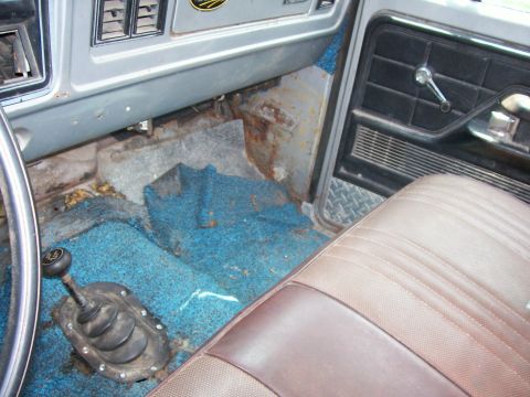 1990 Ford Bronco - The interior of this vintage truck shows significant wear and rust, particularly around the floor and transmission tunnel.