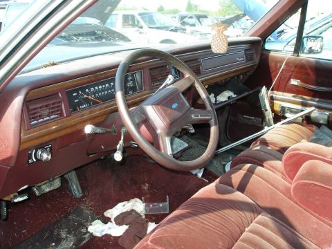 1998 Ford Crown Victoria - The interior of a worn vehicle shows plush velour seats and a dashboard with wood grain accents.