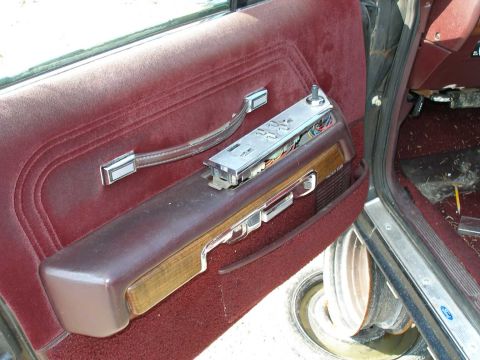 1998 Ford Crown Victoria - The interior door panel of a car shows signs of disrepair with exposed wiring and missing trim pieces.