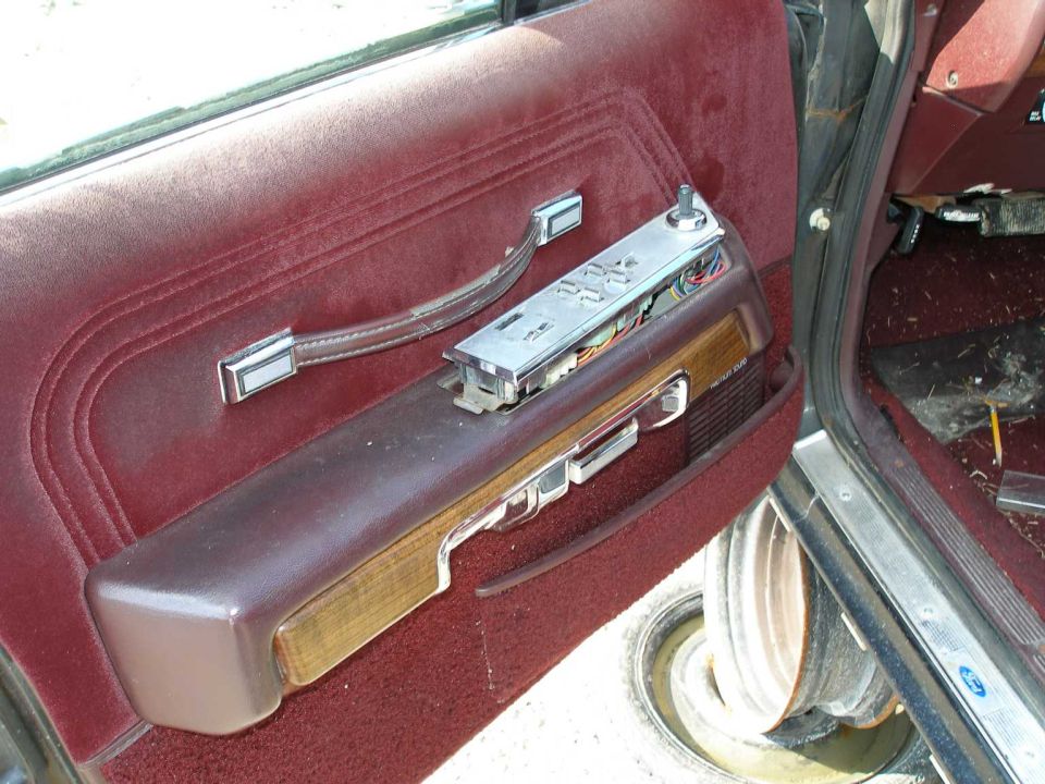 Maroon car door panel with chrome handle, woodgrain trim, and switch panel