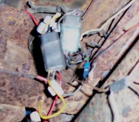 1978 Ford Bronco - A close-up view of a vehicle's wiring harness, showing various connectors and colored wires attached to a rusty metal frame.
