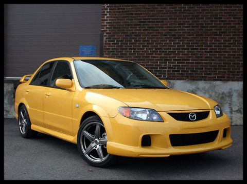 1996 Ford Probe - This yellow sedan features a sporty body kit and custom wheels, parked outdoors.
