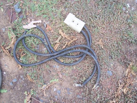 1983 Ford Bronco - A set of jumper cables lies on the ground, a large white connector and metal clamps.