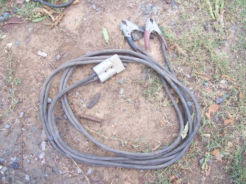 1983 Ford Bronco - Jumper cables with alligator clips and a large connector are coiled on the ground.
