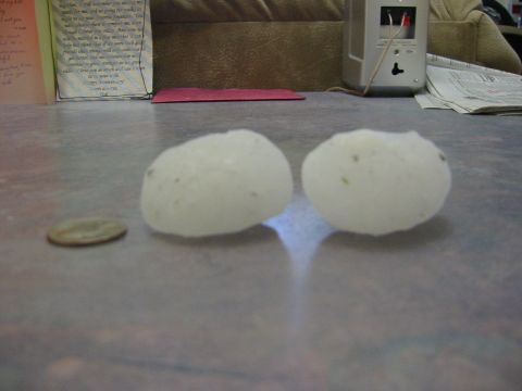 1996 Ford Bronco - Two large hailstones sit next to a coin on a flat surface, with papers and a couch in the background.