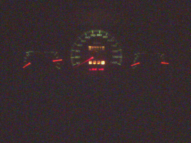 Dark instrument cluster with glowing speedometer and red needles at night