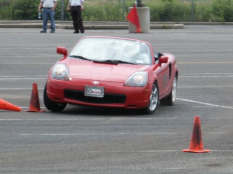 2001 Mercury Grand Marquis - A red convertible sports car is shown on a track, maneuvering around orange cones during what appears to be a driving event.