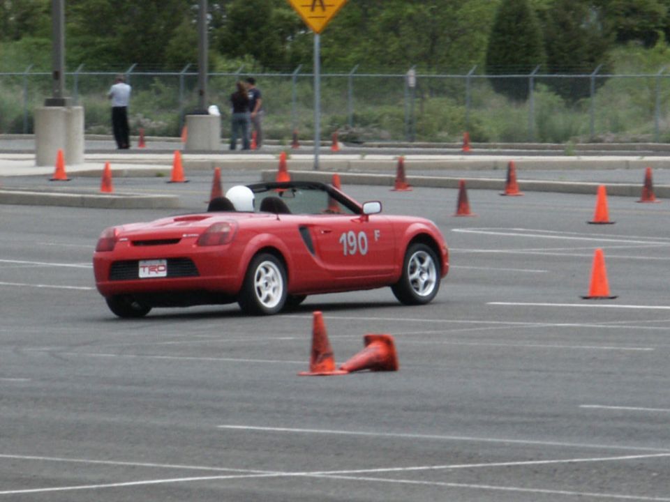Red convertible sports car with number 190 on door, driving on a track with cones