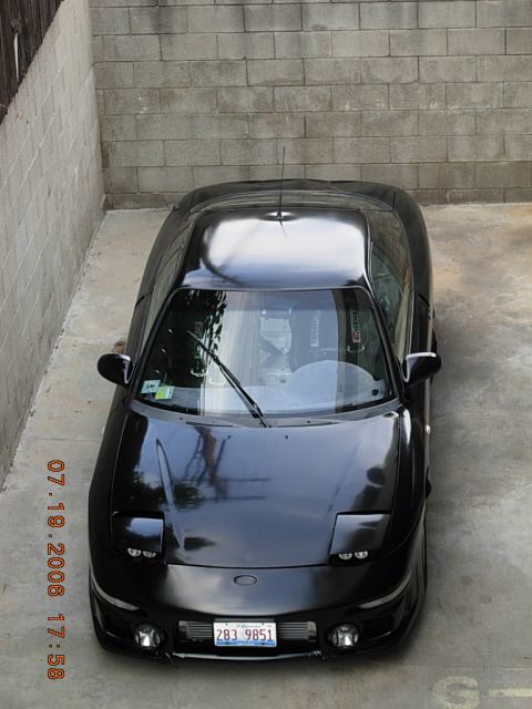 1993 Ford Probe - A black sports car is shown from a high angle, parked in a concrete area next to a brick wall.
