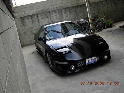 1993 Ford Probe - A black 1993 Ford Probe is parked in front of a brick wall, with a bicycle visible in the background.