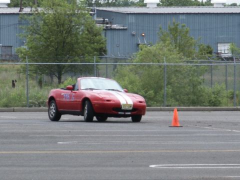 2001 Mercury Grand Marquis - A red convertible with white racing stripes is on a paved surface, possibly a track, with an orange cone in the foreground.