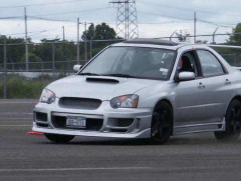 2001 Mercury Grand Marquis - A silver Subaru Impreza WRX STI is seen from the front-three-quarter view on a track.