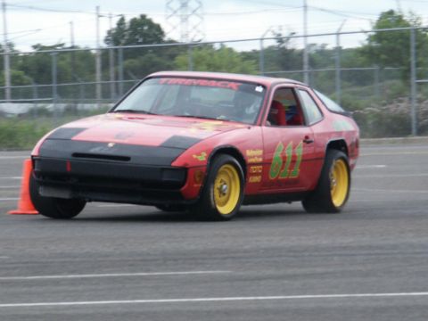 2001 Mercury Grand Marquis - A red race car with yellow wheels and racing decals navigates a track, indicated by an orange cone.