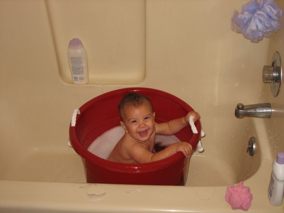 Smiling baby sitting in a red bucket inside a tan bathtub