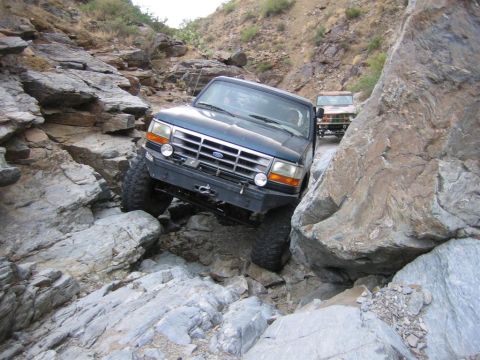 1994 Ford Bronco - Two SUVs tackle a challenging rocky terrain, with the lead vehicle carefully maneuvering through large boulders.