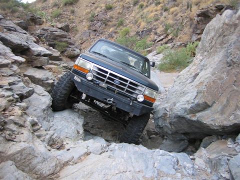 1994 Ford Bronco - A dark blue Ford Bronco maneuvers through a challenging rocky terrain, demonstrating its off-road capabilities.