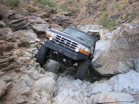 1994 Ford Bronco - A dark blue Ford Bronco tackles a challenging rocky terrain, with a second vehicle following on the trail.
