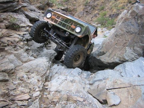 1994 Ford Bronco - A modified off-road vehicle navigates a challenging rocky trail, with its tires angled on steep inclines.