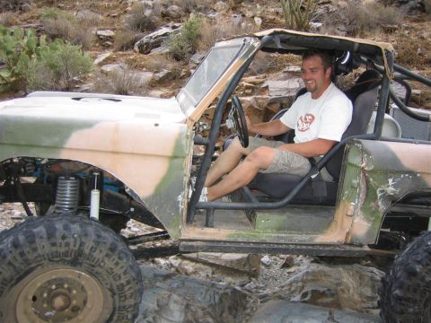 1994 Ford Bronco - Modified SUV with roll cage and camouflage paint sits on rocky terrain with a driver inside.