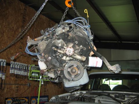 1992 Ford Bronco - A V8 engine suspended from a chain hoist inside a garage, still fitted with spark plug wires, a white Motorcraft oil filter, wiring harness…