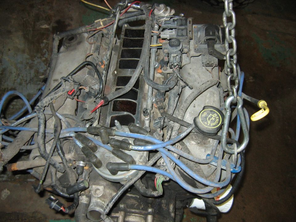 Removed engine on shop floor with blue plug wires and lifting chain