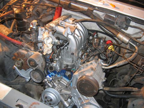 1992 Ford Bronco - Overhead view of a freshly rebuilt V8 engine bay showing a silver/aluminum intake manifold, refinished accessory brackets, alternator, A/C…