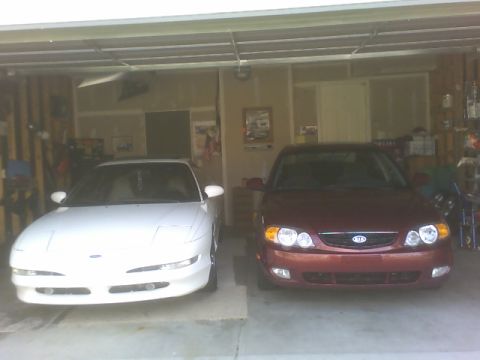 1996 Ford Probe - Two cars are parked side-by-side inside a garage, with the red car on the right displaying a Kia emblem.