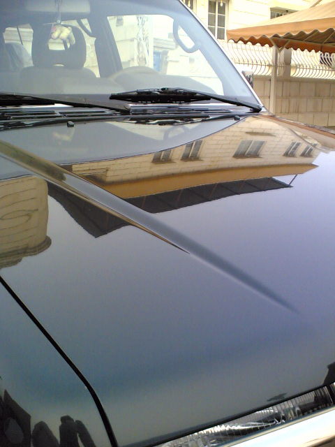 2000 Mitsubishi Montero - Hood and windshield of a dark 2000 Mitsubishi Montero, reflecting a building.