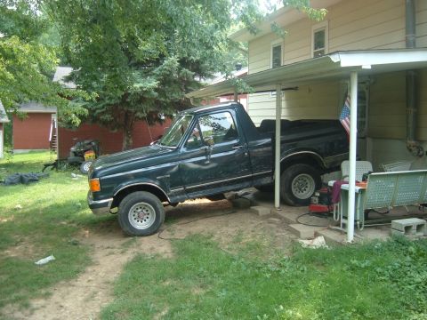 1988 Ford Bronco - A dark green pickup truck is parked at an angle under a covered patio area.